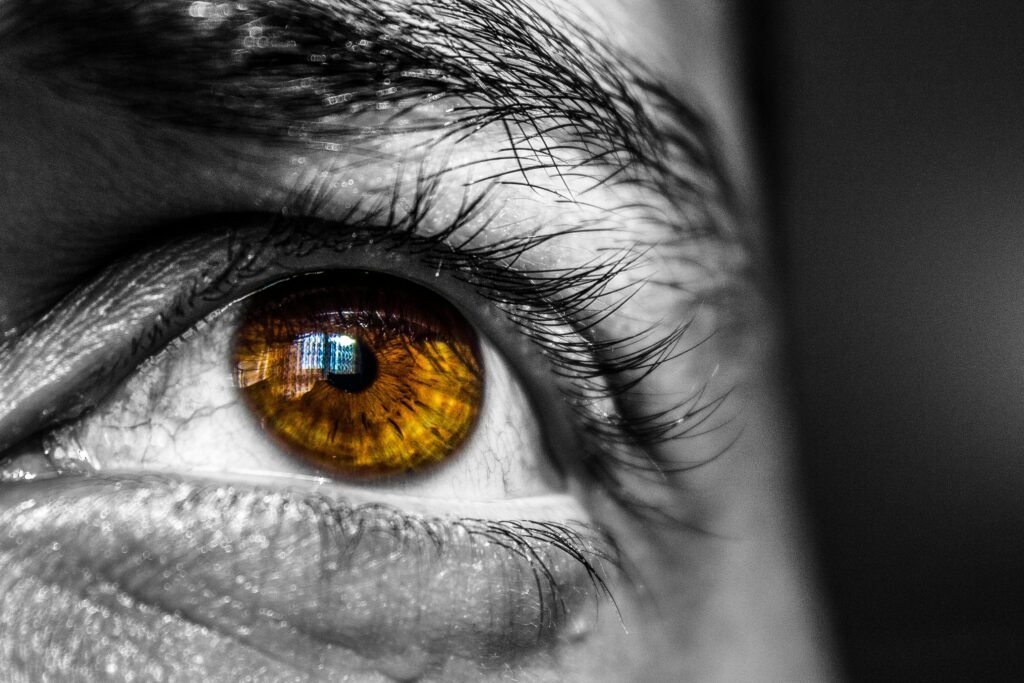 Detailed close-up image of a human eye, showcasing an amber-colored iris with architectural reflection.